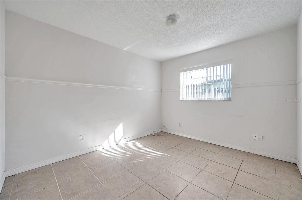 An empty bedroom features white walls with chair rail molding, tile flooring, and a window — 1005 LAKE PALMS DRIVE, LARGO, FL