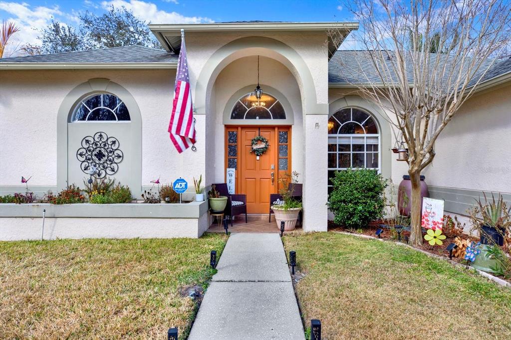 The exterior of a single-story home features a tan stucco facade, arched windows, and an orange door — 9656 FOX HEARST ROAD, TAMPA, FL