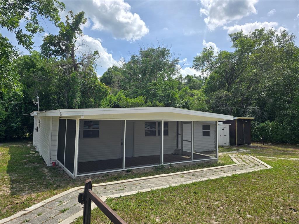 A white house with a large screened-in porch sits on a grassy lot with trees — 10566 E RABBIT LANE, FLORAL CITY, FL