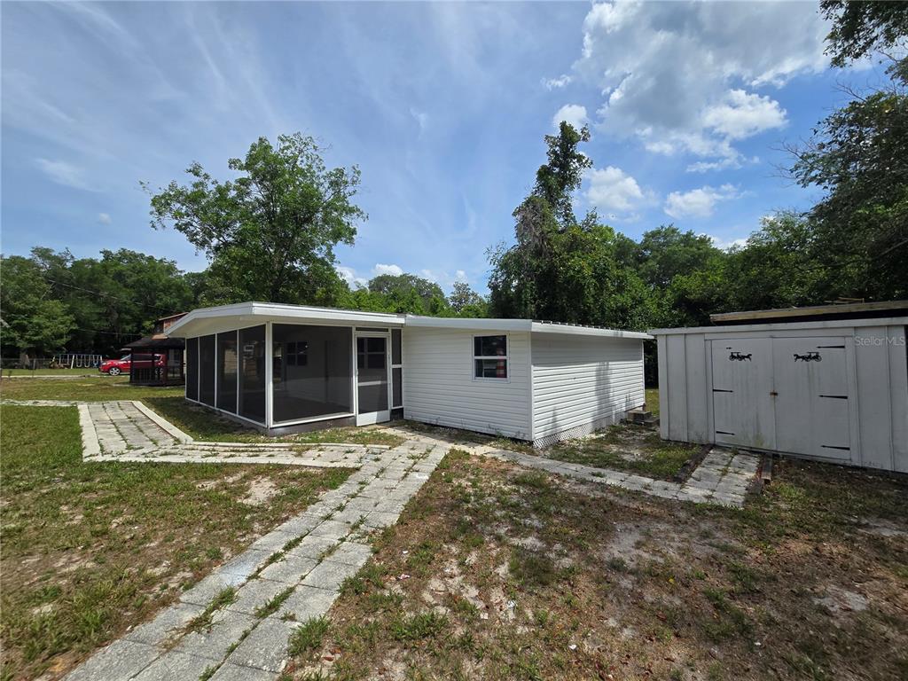 A white house with a screened-in porch and a detached shed in a grassy yard — 10566 E RABBIT LANE, FLORAL CITY, FL
