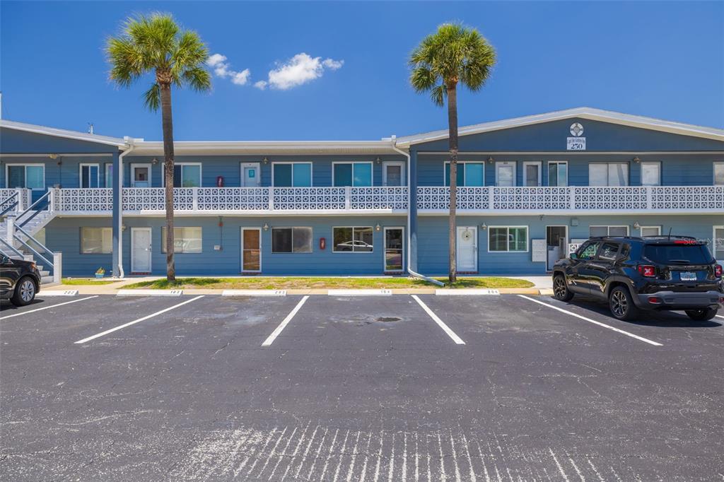 A two-story blue apartment building with a parking lot and two palm trees in front — 250 126TH AVENUE UNIT 104, TREASURE ISLAND, FL