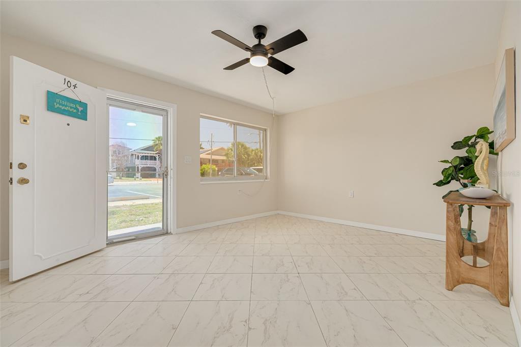 An empty room with white marble-look tile floors, a ceiling fan, and a glass door — 250 126TH AVENUE UNIT 104, TREASURE ISLAND, FL