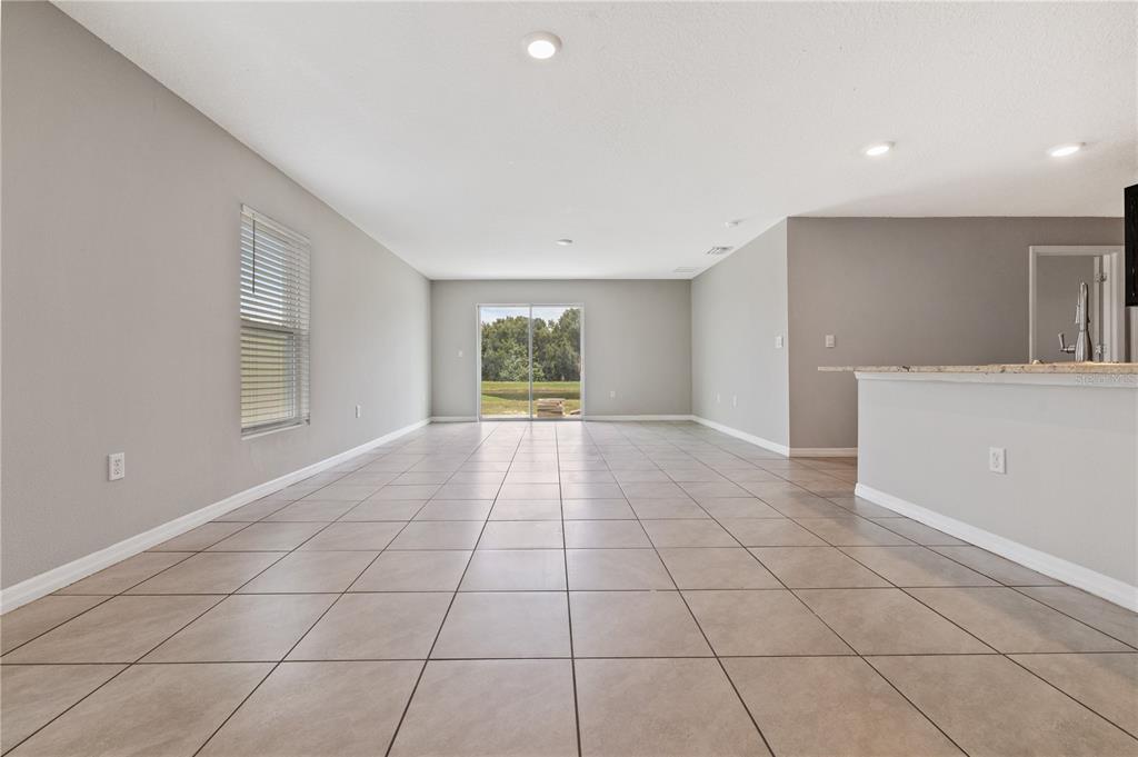 A spacious living area features light gray walls, large beige floor tiles, and a sliding door — 11722 WHITE WILLOW LANE, RIVERVIEW, FL