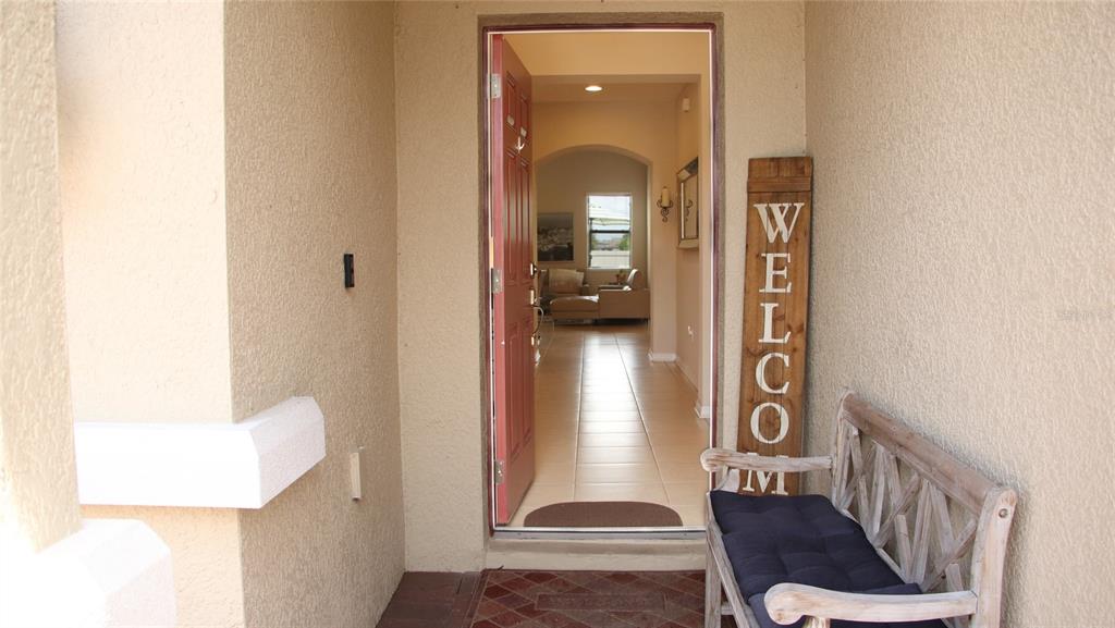 A front porch features a wooden bench and a vertical welcome sign beside an open door — 1429 CLEAR BROOK PLACE, ST CLOUD, FL