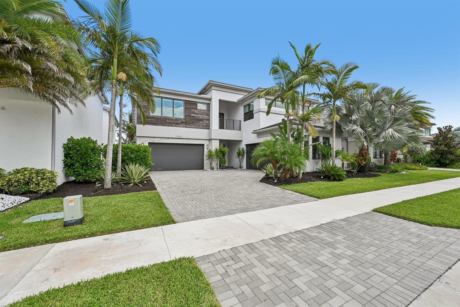 A modern two-story house with a gray garage, wood-paneled accents, and palm trees — 17070 Rainbow Falls Trail, Boca Raton FL 33496, BOCA RATON, FL