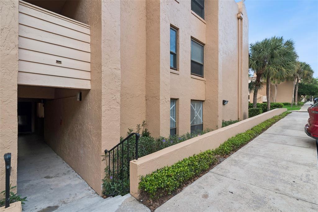 An exterior view of a tan stucco apartment building with a covered walkway and landscaping — 530 CRANES WAY UNIT 107, ALTAMONTE SPRINGS, FL