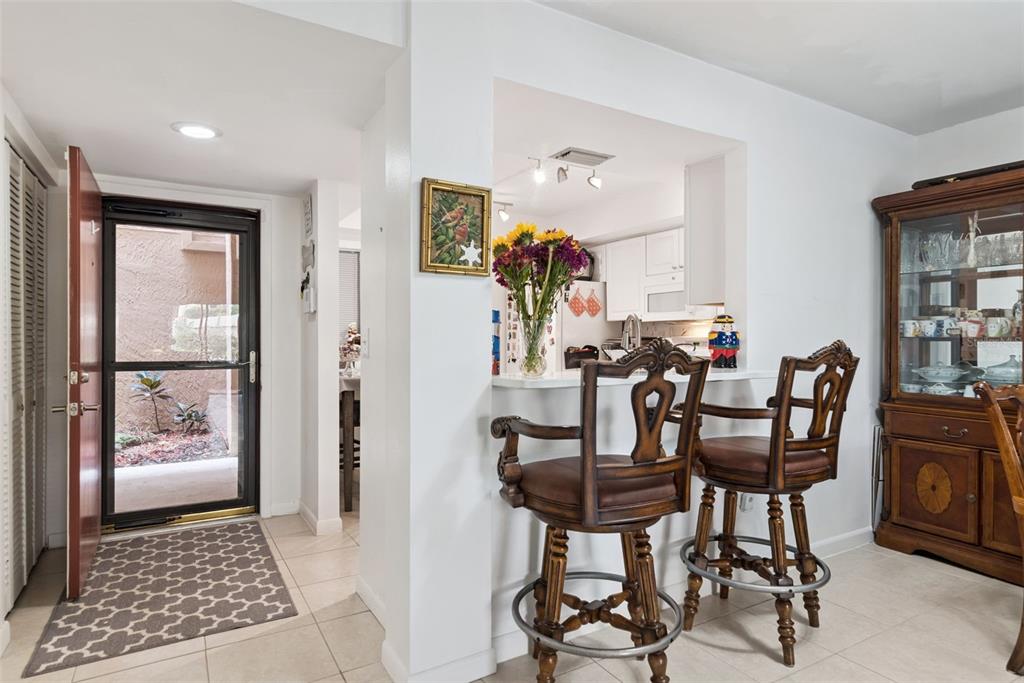 A kitchen pass-through with bar stools overlooks a dining area near an open front door — 530 CRANES WAY UNIT 107, ALTAMONTE SPRINGS, FL