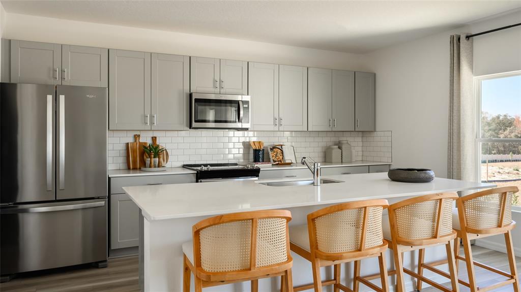 A modern kitchen features gray cabinets, white countertops, a central island, and three wooden stools — 9255 ORCHARD PARK LANE, ZEPHYRHILLS, FL