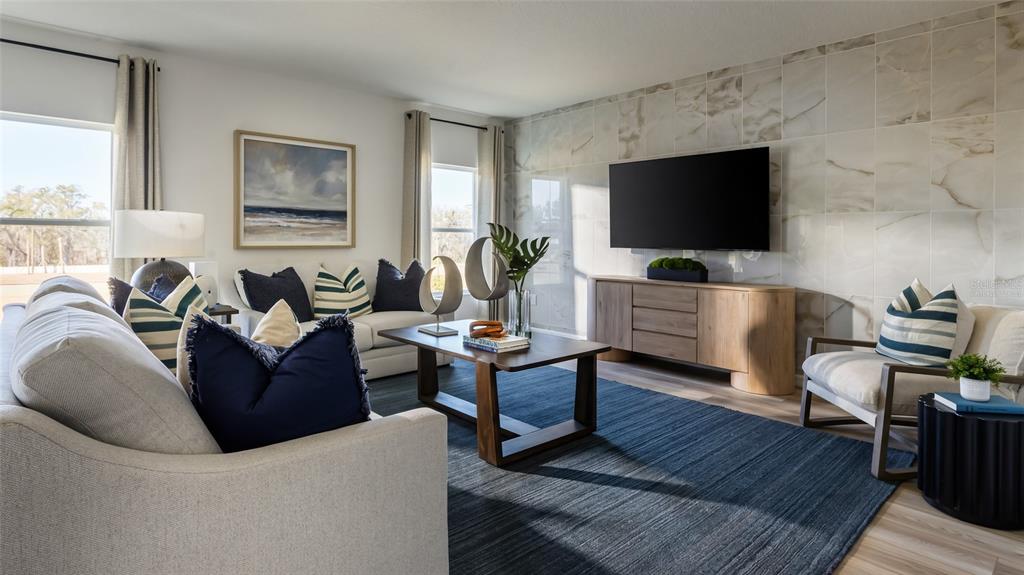 A living room features a marble-tiled accent wall, a large television, and a blue rug — 9255 ORCHARD PARK LANE, ZEPHYRHILLS, FL
