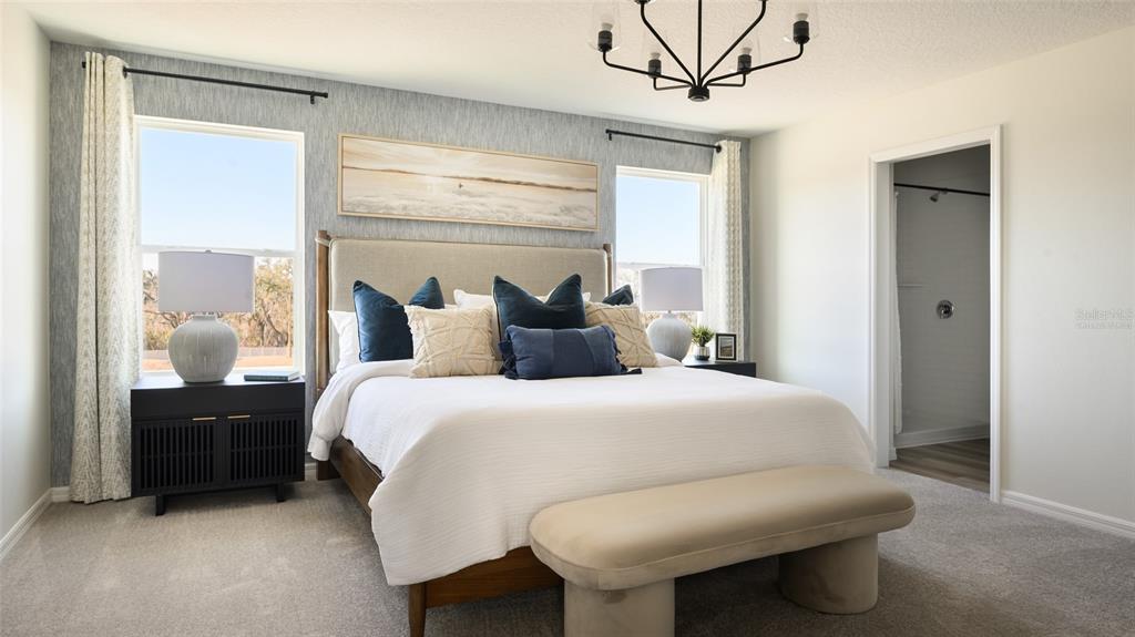 A bedroom features a bed with blue and beige pillows, a bench, and two windows — 9255 ORCHARD PARK LANE, ZEPHYRHILLS, FL