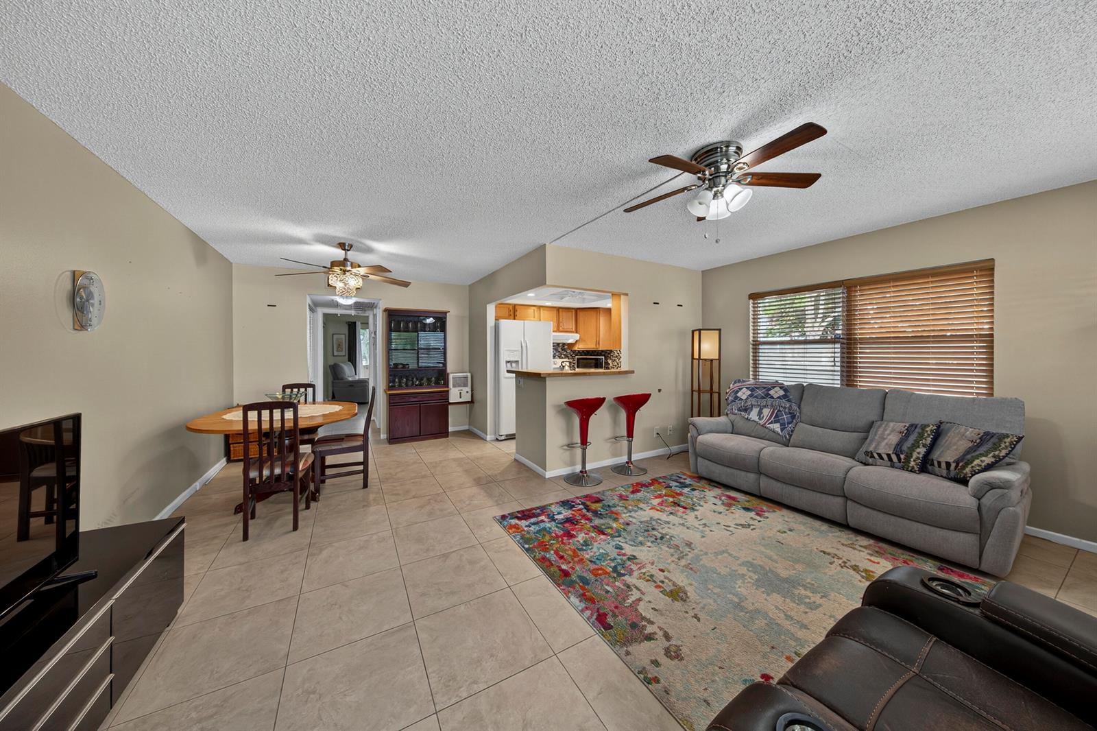 An open-concept living and dining area features tile flooring, a kitchen breakfast bar, and ceiling fans — 125 Newport I, Deerfield Beach FL 33442, DEERFIELD BEACH, FL