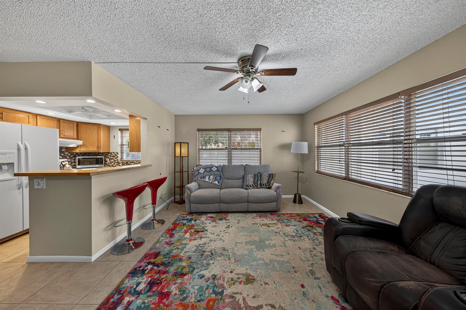 A living room with a gray sofa, a colorful area rug, and an adjacent kitchen bar — 125 Newport I, Deerfield Beach FL 33442, DEERFIELD BEACH, FL