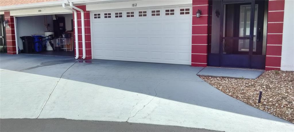 A two-car garage with a white door sits beside a front entrance with red trim — 1812 ATRIUM DRIVE, SUN CITY CENTER, FL