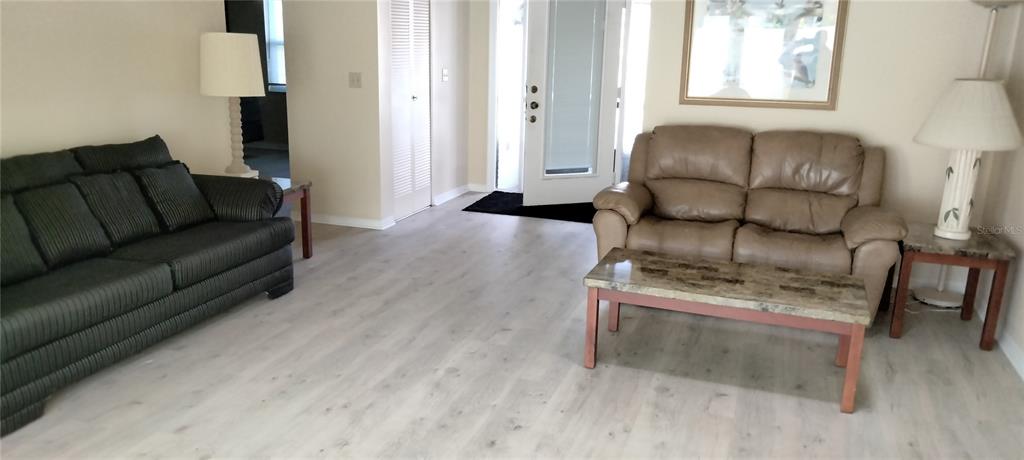 A living room features light wood-look flooring, a dark sofa, and a tan loveseat — 1812 ATRIUM DRIVE, SUN CITY CENTER, FL