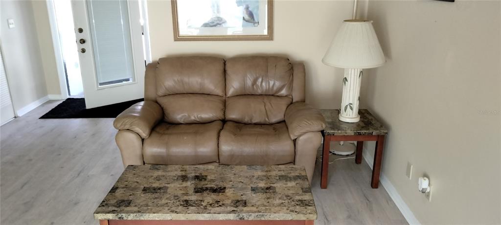 A tan leather loveseat sits in a room with light wood floors and a side table — 1812 ATRIUM DRIVE, SUN CITY CENTER, FL