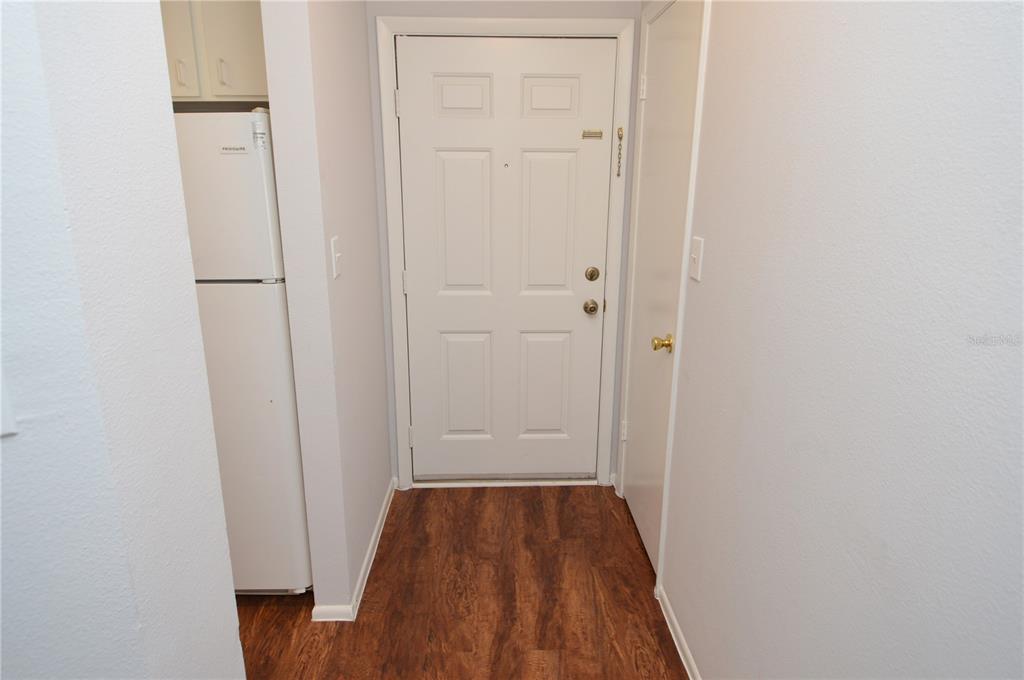 A white front door opens into a small entryway with wood-look flooring and a refrigerator — 8625 MALLARD RESERVE DRIVE UNIT 201, TAMPA, FL