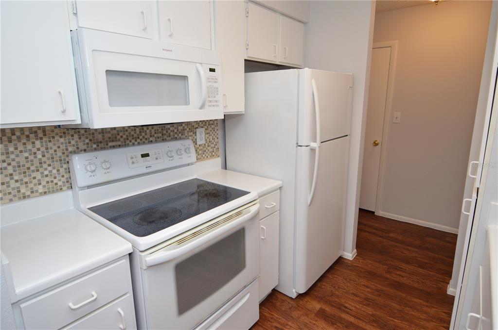 A kitchen with white cabinets, white appliances, a glass-top stove, and a mosaic tile backsplash — 8625 MALLARD RESERVE DRIVE UNIT 201, TAMPA, FL