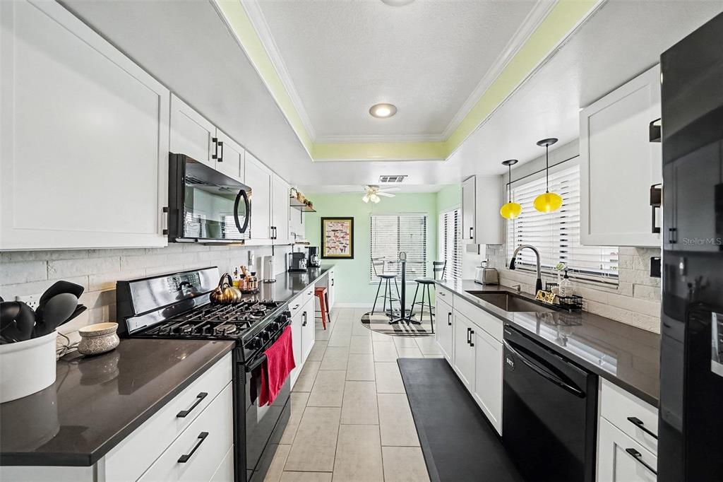A galley-style kitchen features white cabinets, dark countertops, black appliances, and light green accent walls — 144 SPOONHOUR DRIVE, CASSELBERRY, FL