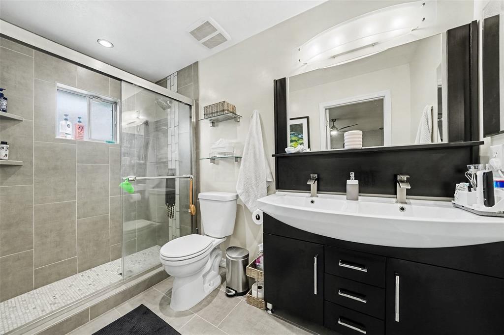 A bathroom features a glass-enclosed shower, a white toilet, and a black double-sink vanity — 144 SPOONHOUR DRIVE, CASSELBERRY, FL