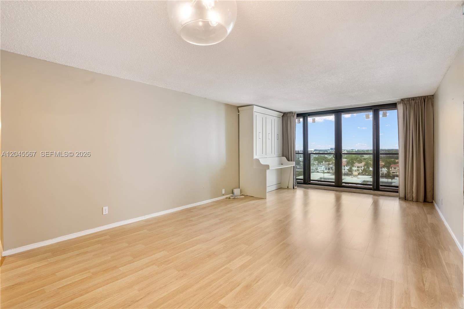 An empty room features light wood flooring, beige walls, a white wall bed, and floor-to-ceiling windows — 2301 S Ocean Dr # 1006, Hollywood FL 33019, HOLLYWOOD, FL