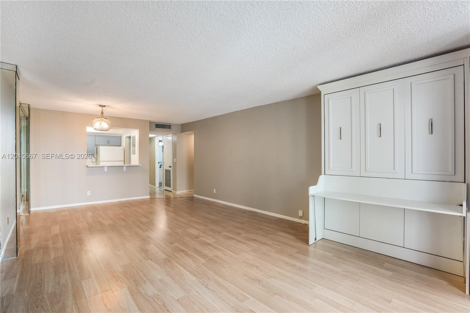 A living room features light wood flooring, beige walls, and a white wall-mounted Murphy bed — 2301 S Ocean Dr # 1006, Hollywood FL 33019, HOLLYWOOD, FL