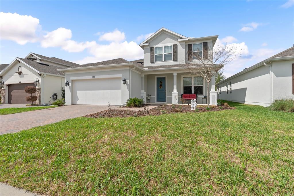 A two-story suburban house with a white garage, blue front door, and a grassy lawn — 693 BIG PINE AVENUE, MINNEOLA, FL