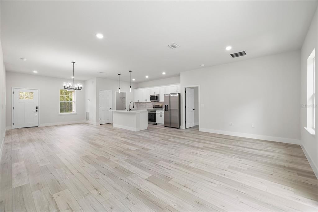 An open-concept kitchen and living area features white cabinets, stainless steel appliances, and wood-look flooring — 8555 N TROJAN DRIVE, CITRUS SPRINGS, FL