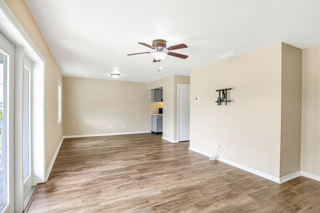 An empty living room features wood-look flooring, beige walls, a ceiling fan, and a kitchen — 4995 COBIA DRIVE SE UNIT D, ST PETERSBURG, FL