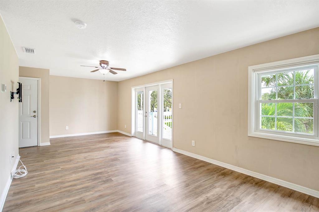 An empty room features light wood-look flooring, beige walls, a ceiling fan, and glass doors — 4995 COBIA DRIVE SE UNIT D, ST PETERSBURG, FL