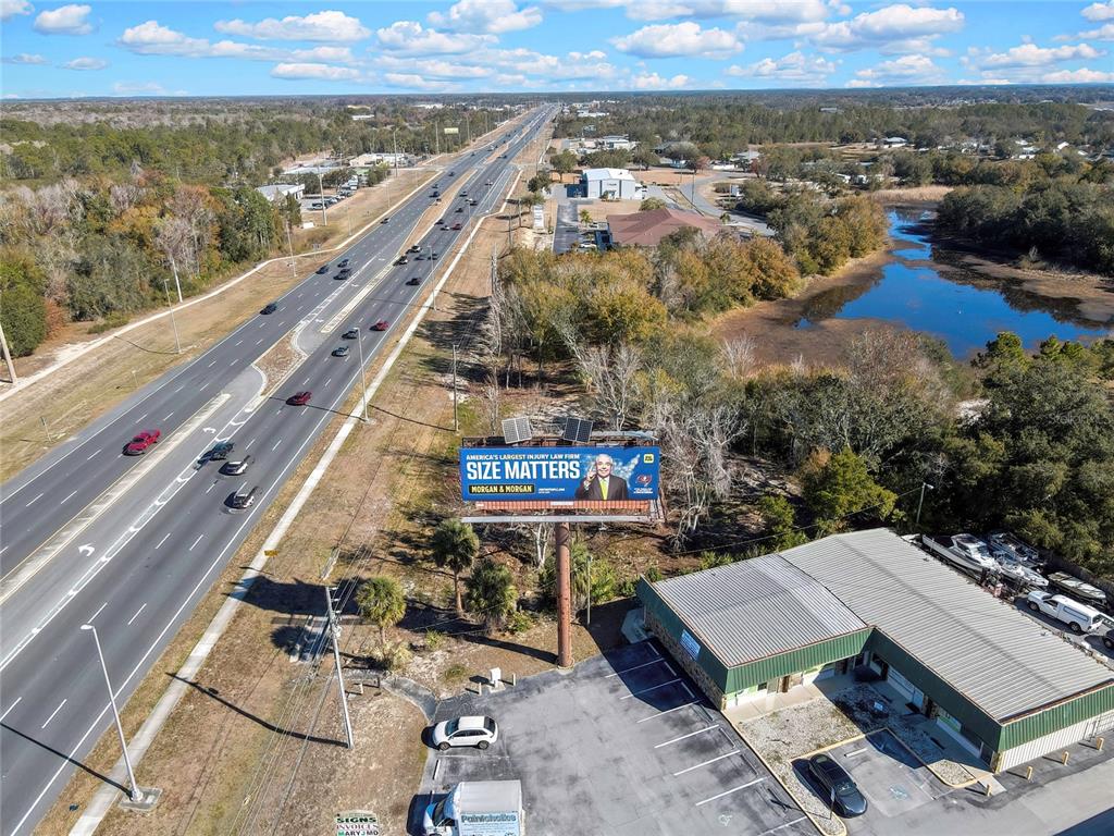 An aerial view shows a highway, a billboard, and a commercial building with a parking lot — 0 COMMERCIAL WAY, SPRING HILL, FL