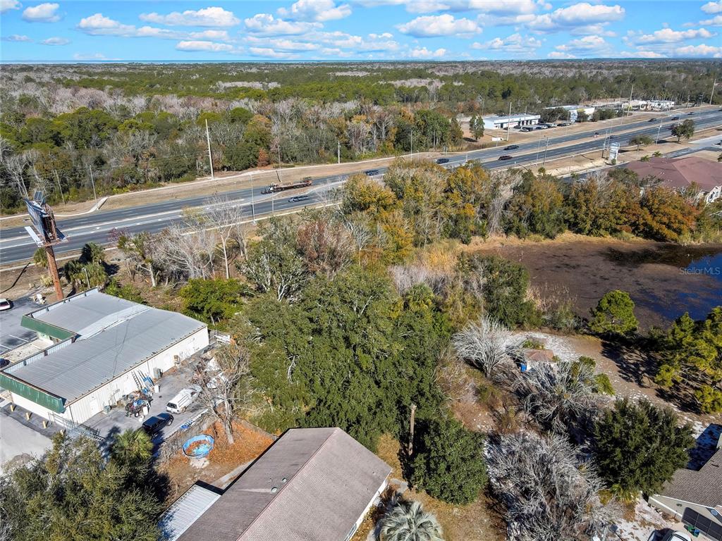 An aerial view shows a commercial building, a residential roof, trees, and a nearby highway — 0 COMMERCIAL WAY, SPRING HILL, FL