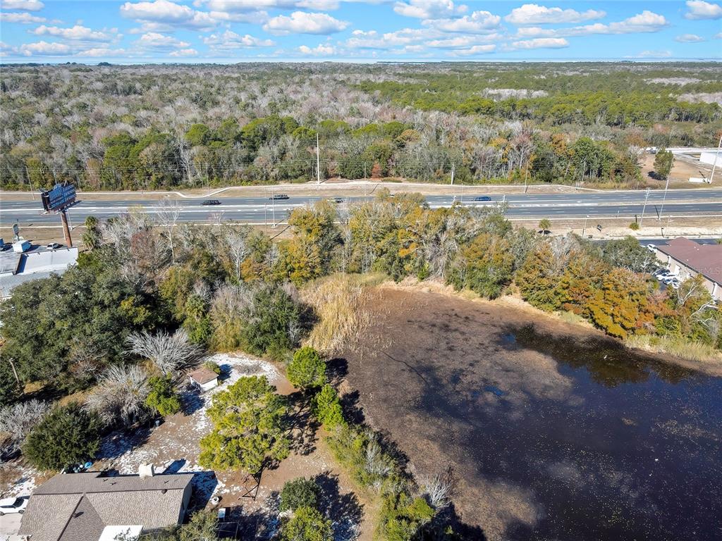 An aerial view shows a pond, surrounding trees, a house, and a nearby highway — 0 COMMERCIAL WAY, SPRING HILL, FL