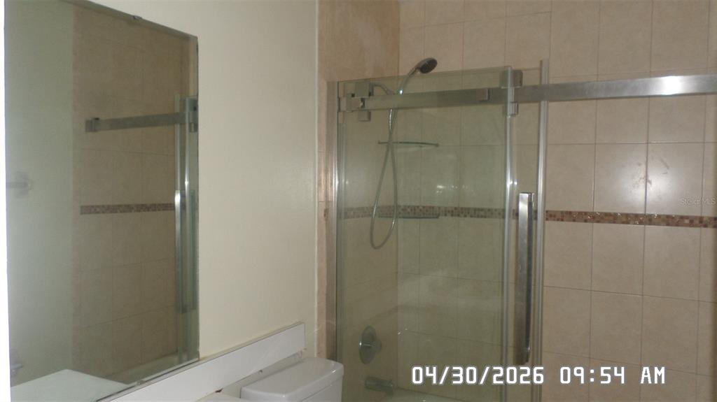 A bathroom features a glass-enclosed shower with tiled walls and a wall-mounted mirror — 2665 MILL RUN BOULEVARD, KISSIMMEE, FL