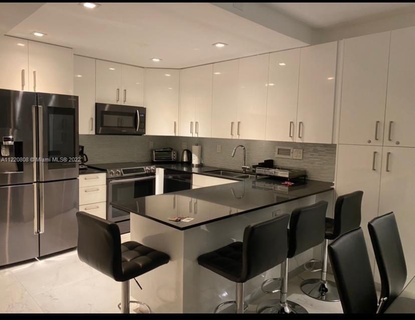 A modern kitchen features white glossy cabinets, black countertops, stainless steel appliances, and bar seating — 2301 Collins Ave # 1503, Miami Beach FL 33139, MIAMI BEACH, FL