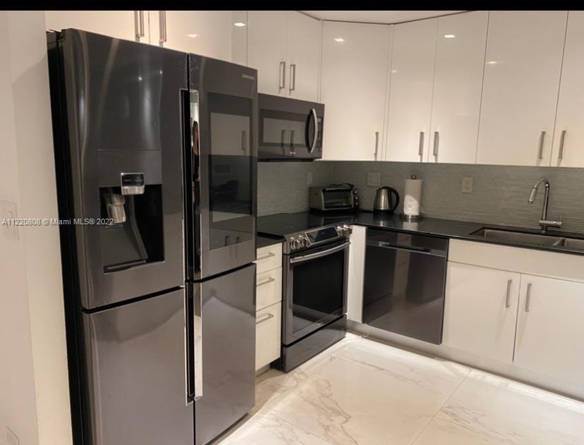 A modern kitchen features white cabinets, black appliances, and light-colored marble-patterned tile flooring — 2301 Collins Ave # 1503, Miami Beach FL 33139, MIAMI BEACH, FL