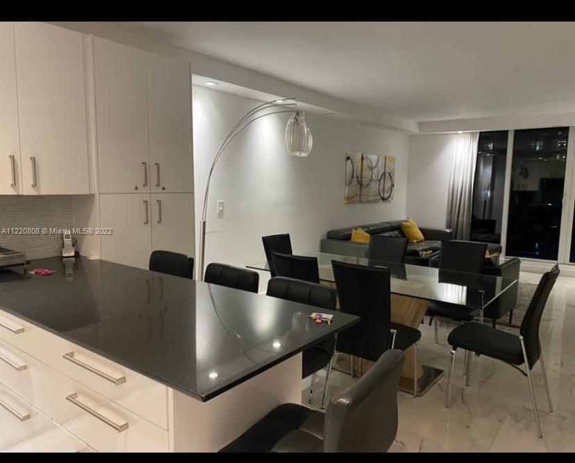 A modern kitchen with black countertops and white cabinets opens into a dining and living area — 2301 Collins Ave # 1503, Miami Beach FL 33139, MIAMI BEACH, FL