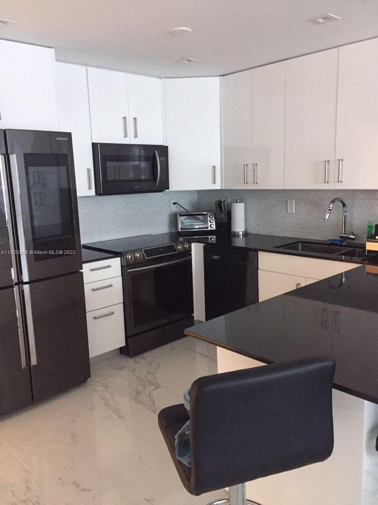 A modern kitchen features white cabinets, black countertops, stainless steel appliances, and marble-look flooring — 2301 Collins Ave # 1503, Miami Beach FL 33139, MIAMI BEACH, FL