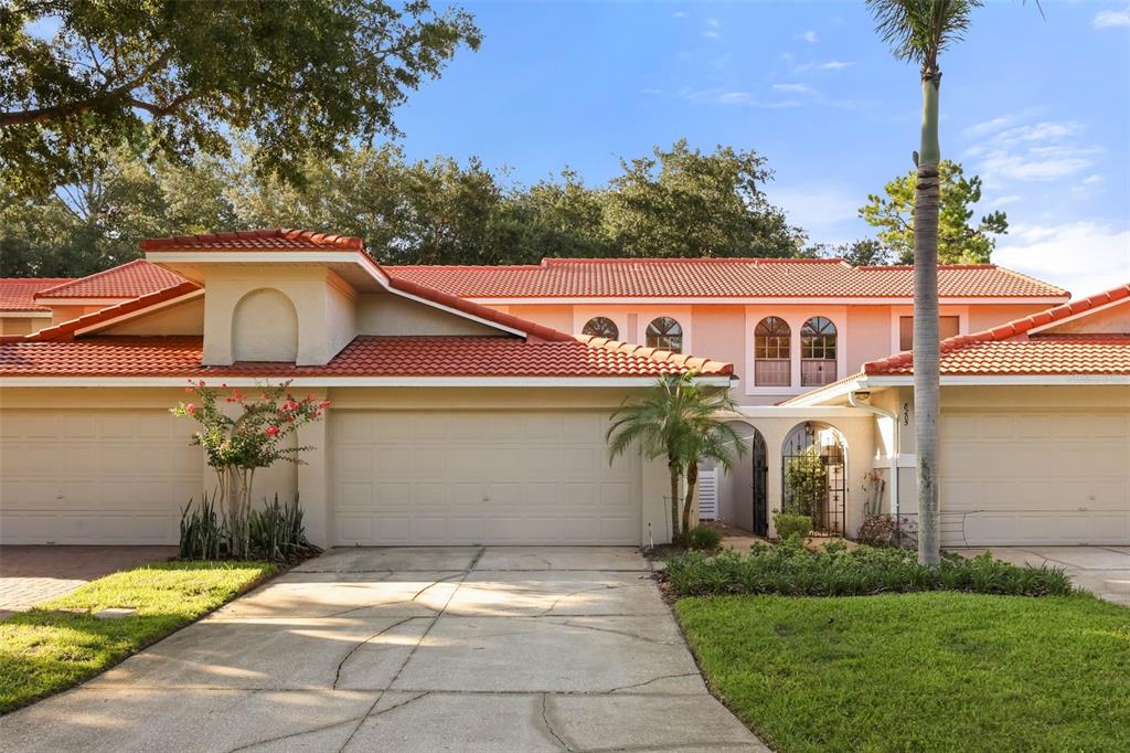 A two-story townhouse with a red tile roof, beige stucco walls, and a concrete driveway — 8209 SANDPOINT BOULEVARD, ORLANDO, FL