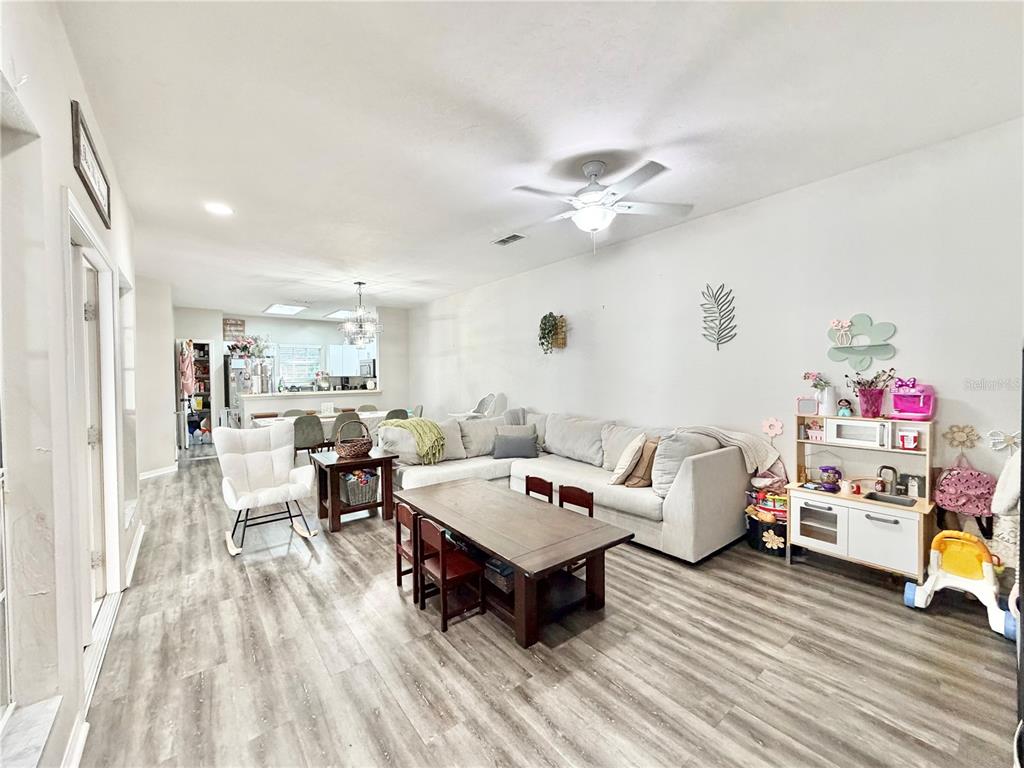 An open-concept living area features light wood-look flooring, a sectional sofa, and a dining table — 7090 NW 52ND TERRACE, GAINESVILLE, FL
