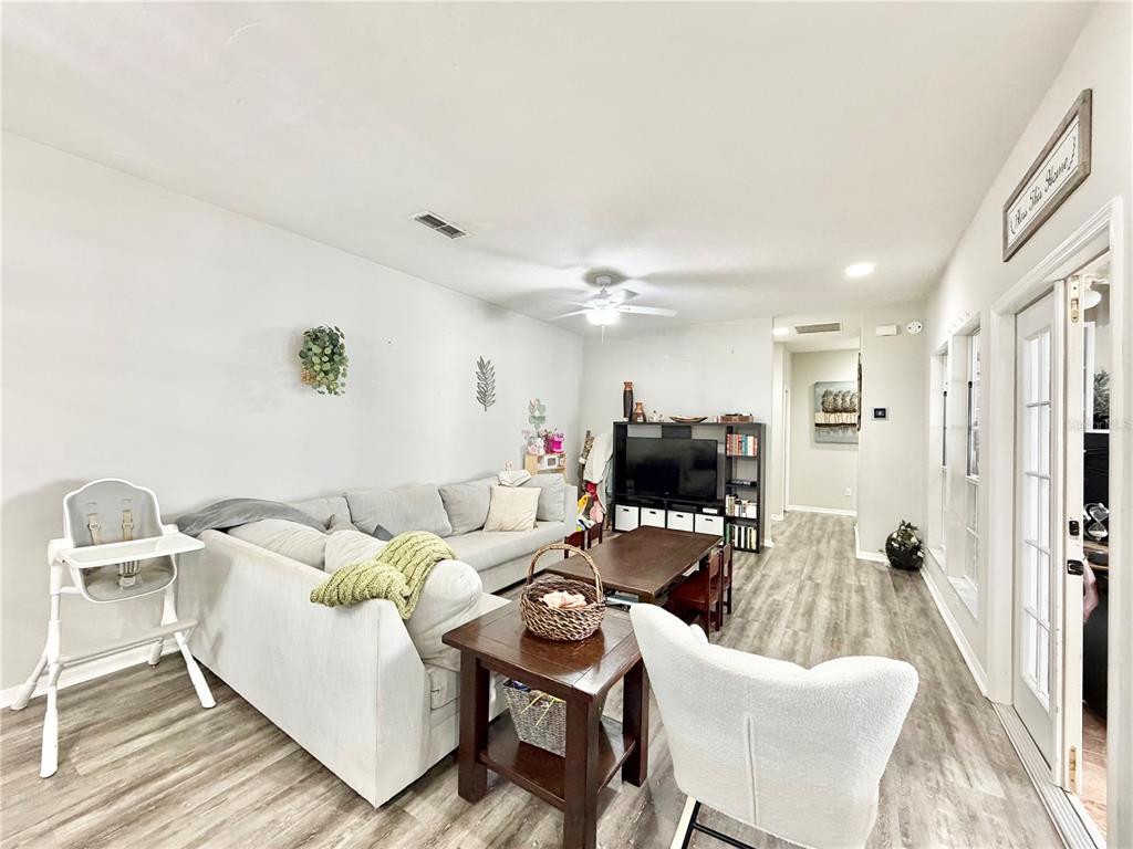 A living room features light gray flooring, a sectional sofa, a television console, and a ceiling fan — 7090 NW 52ND TERRACE, GAINESVILLE, FL