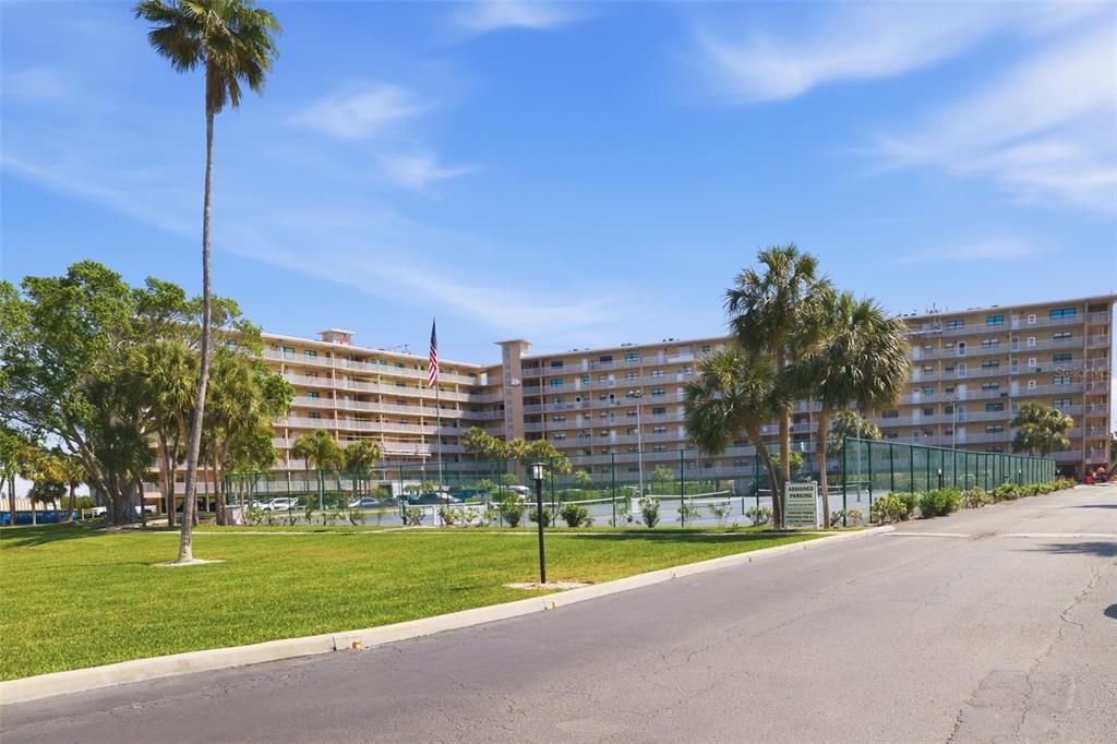 A multi-story apartment building stands behind a tennis court and a grassy lawn — 19451 GULF BOULEVARD UNIT 203, INDIAN SHORES, FL