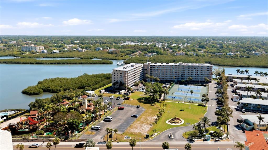 An aerial view shows a multi-story apartment complex with tennis courts and a parking lot — 19451 GULF BOULEVARD UNIT 203, INDIAN SHORES, FL