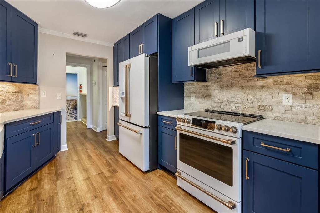 A kitchen features blue cabinets, white appliances, a stone backsplash, and wood-look flooring — 86 FELLOWSHIP DRIVE, PALM COAST, FL