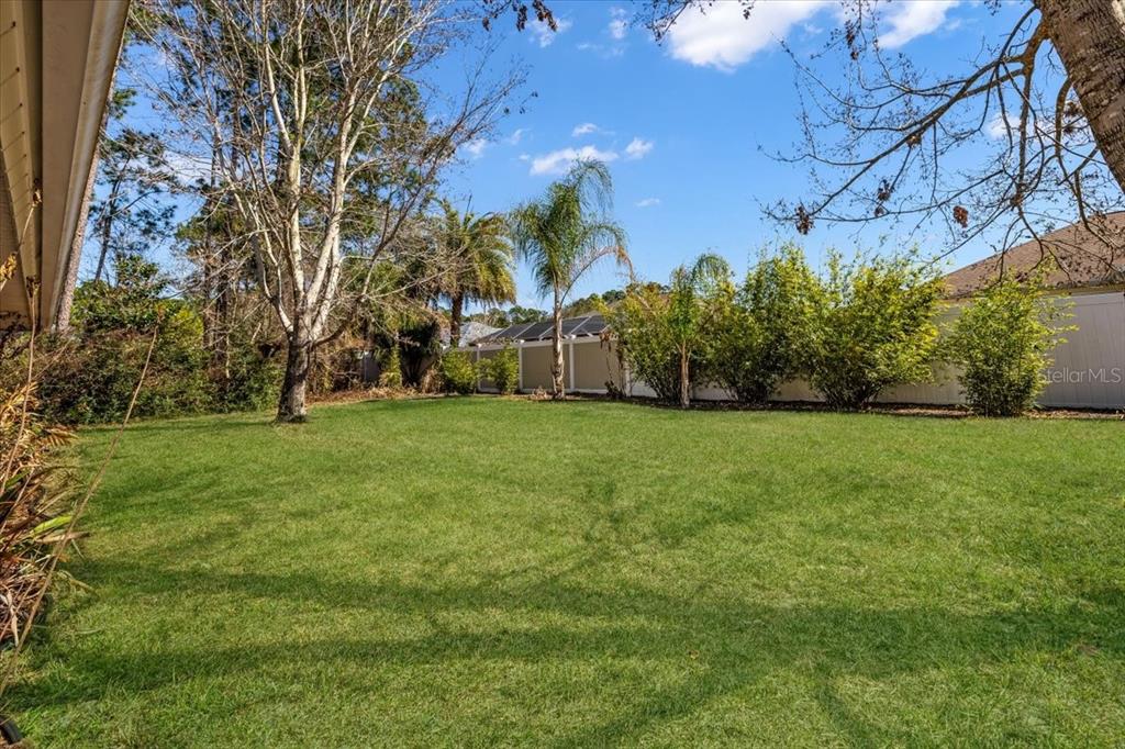 A grassy backyard features trees, palm trees, and a white fence under a blue sky — 86 FELLOWSHIP DRIVE, PALM COAST, FL