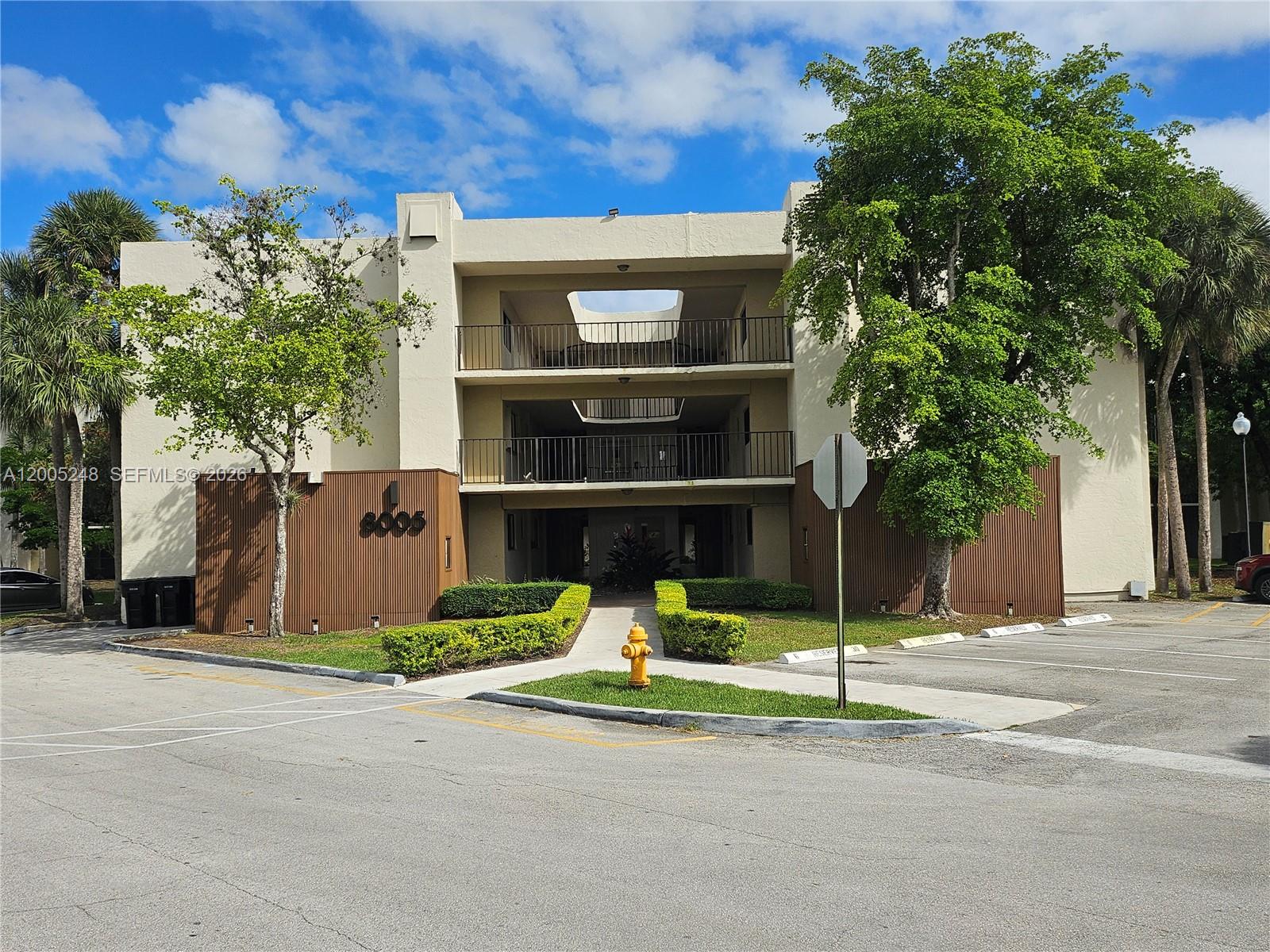 A three-story apartment building features a central open-air walkway, balconies, and a parking lot — 8005 SW 107th Ave # 305, Miami FL 33173, MIAMI, FL