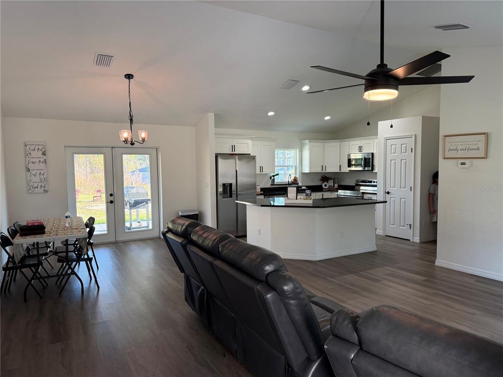 An open-concept kitchen and dining area features white cabinetry, a dark island, and wood-look flooring — 14110 SW 64TH TERRACE ROAD, OCALA, FL