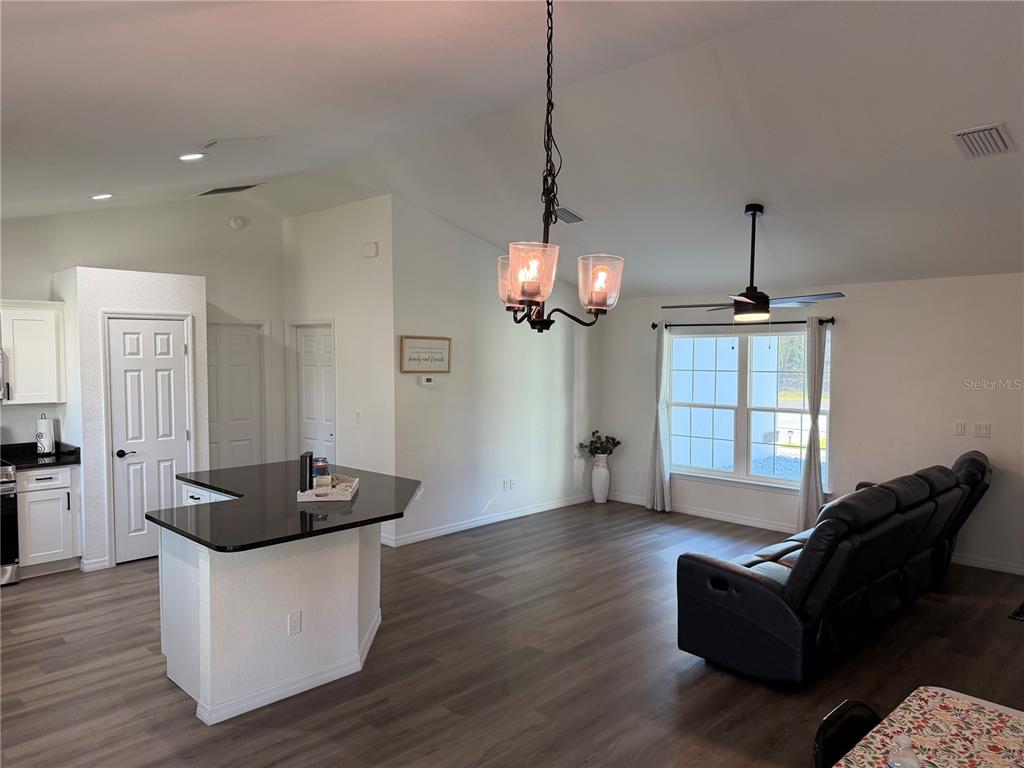 An open-concept living area features a kitchen island, dark flooring, and a dining chandelier — 14110 SW 64TH TERRACE ROAD, OCALA, FL