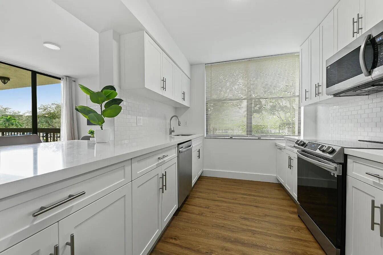A modern white kitchen features subway tile backsplashes, stainless steel appliances, and wood-look flooring — 955 Egret Circle # 211, Delray Beach FL 33444, DELRAY BEACH, FL