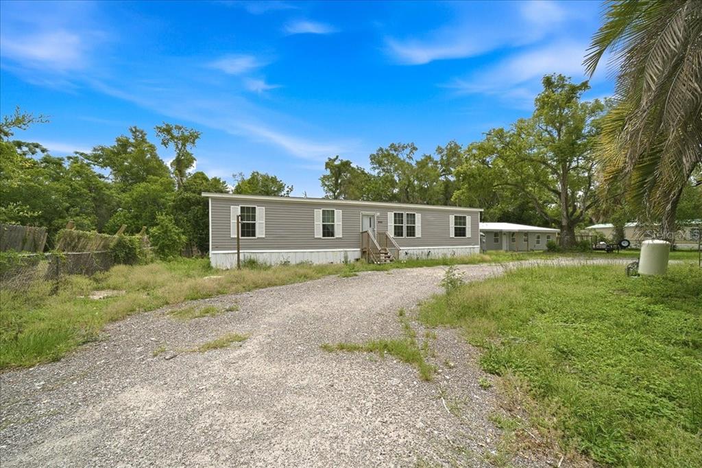 A gray manufactured home sits on a gravel driveway surrounded by trees and grass — 444 KORBUS ROAD, BROOKSVILLE, FL