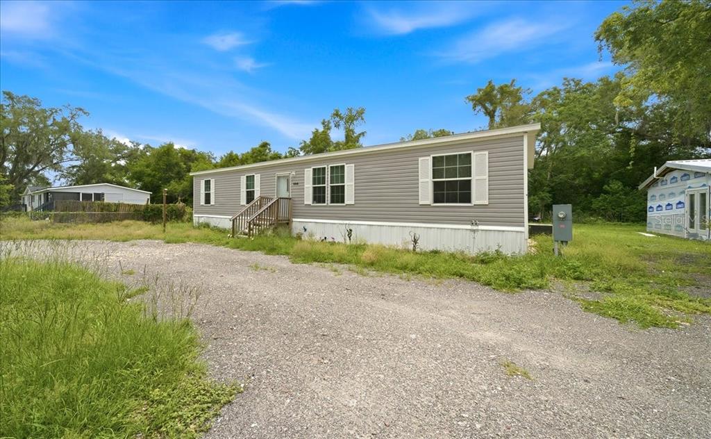 A gray manufactured home with white shutters sits on a gravel lot with trees — 444 KORBUS ROAD, BROOKSVILLE, FL